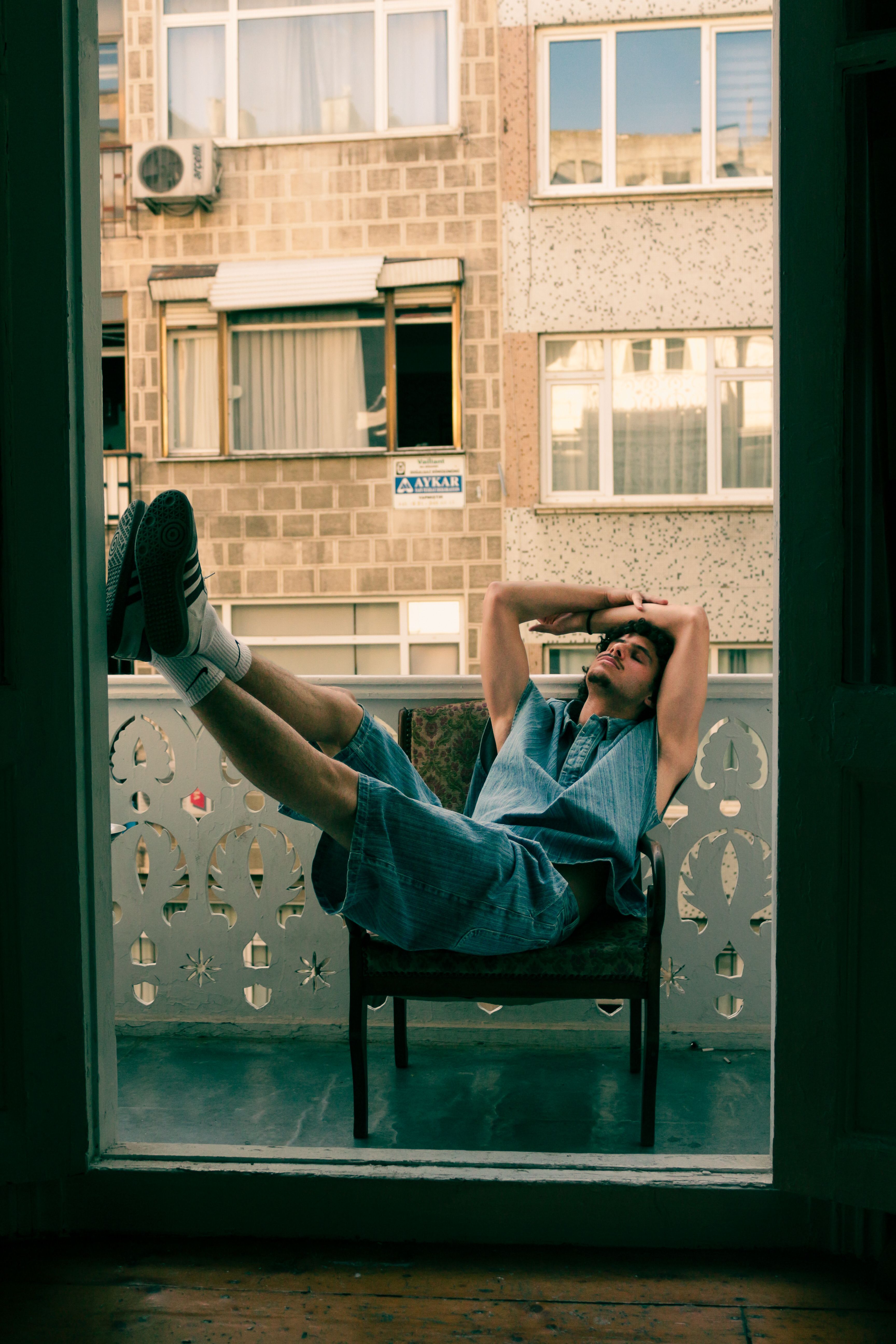 Young man lounging on a balcony chair in a residential urban setting.