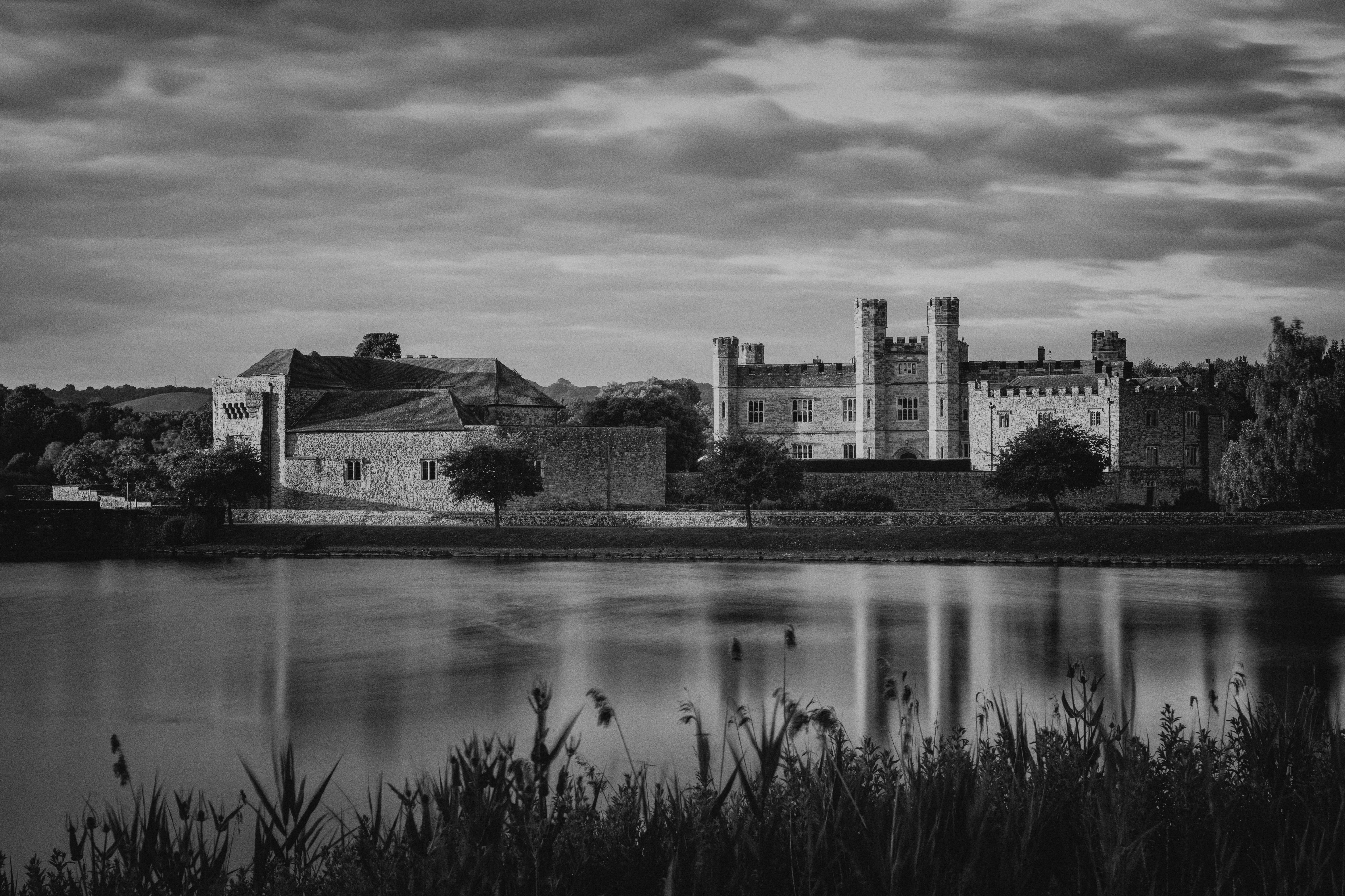 Black and white photo of Leeds Castle reflected in a lake under a cloudy sky.