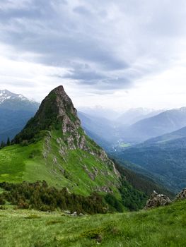 A scenic view of a rocky mountain peak surrounded by lush greenery under an overcast sky.