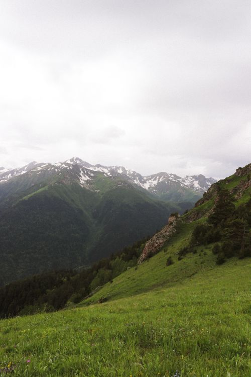 Free Beautiful view of snowcapped mountains under cloudy skies with lush green valley. Stock Photo
