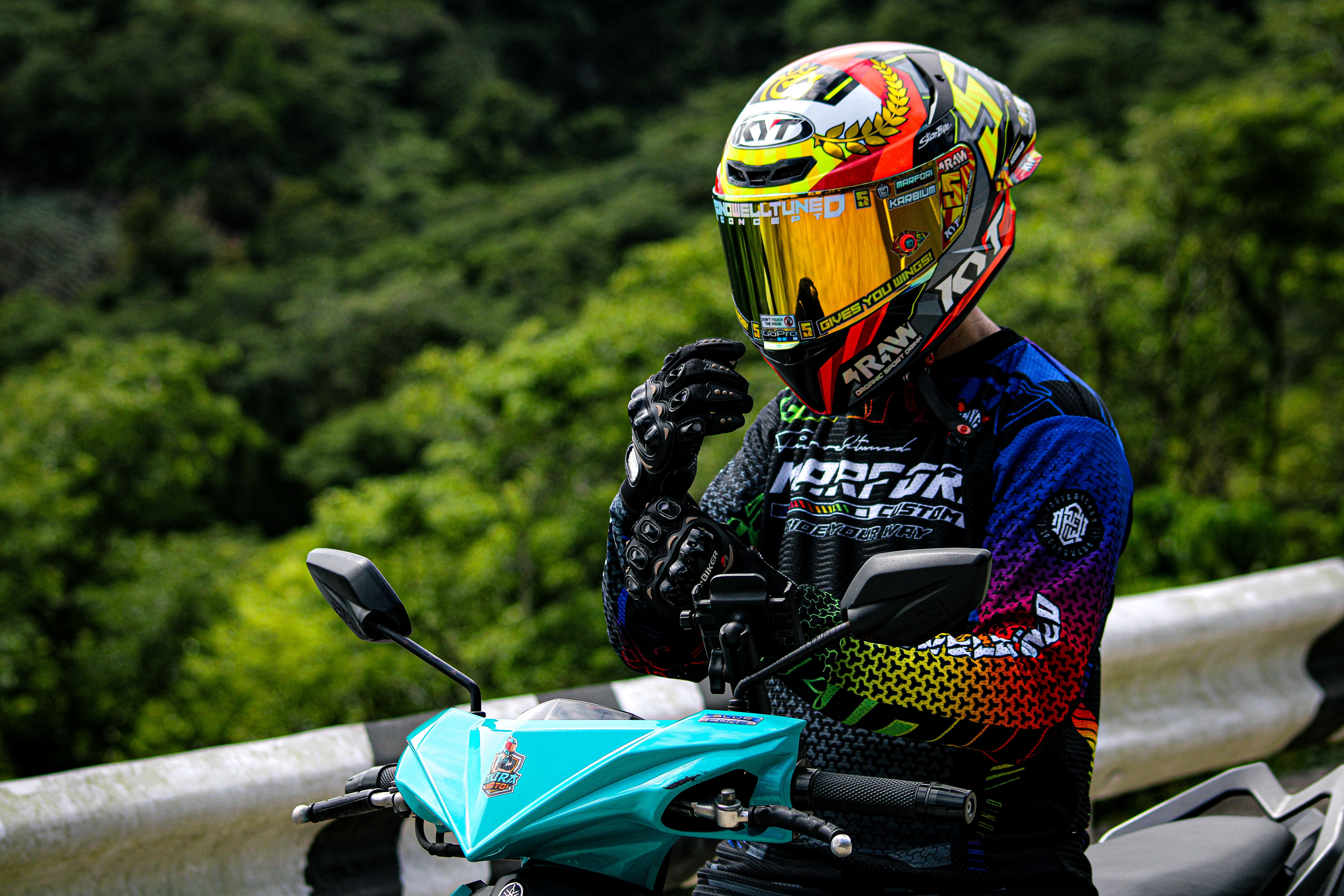 A motorcyclist with a colorful helmet adjusts gear on a bike in the lush greenery of Tabaco City, Philippines.