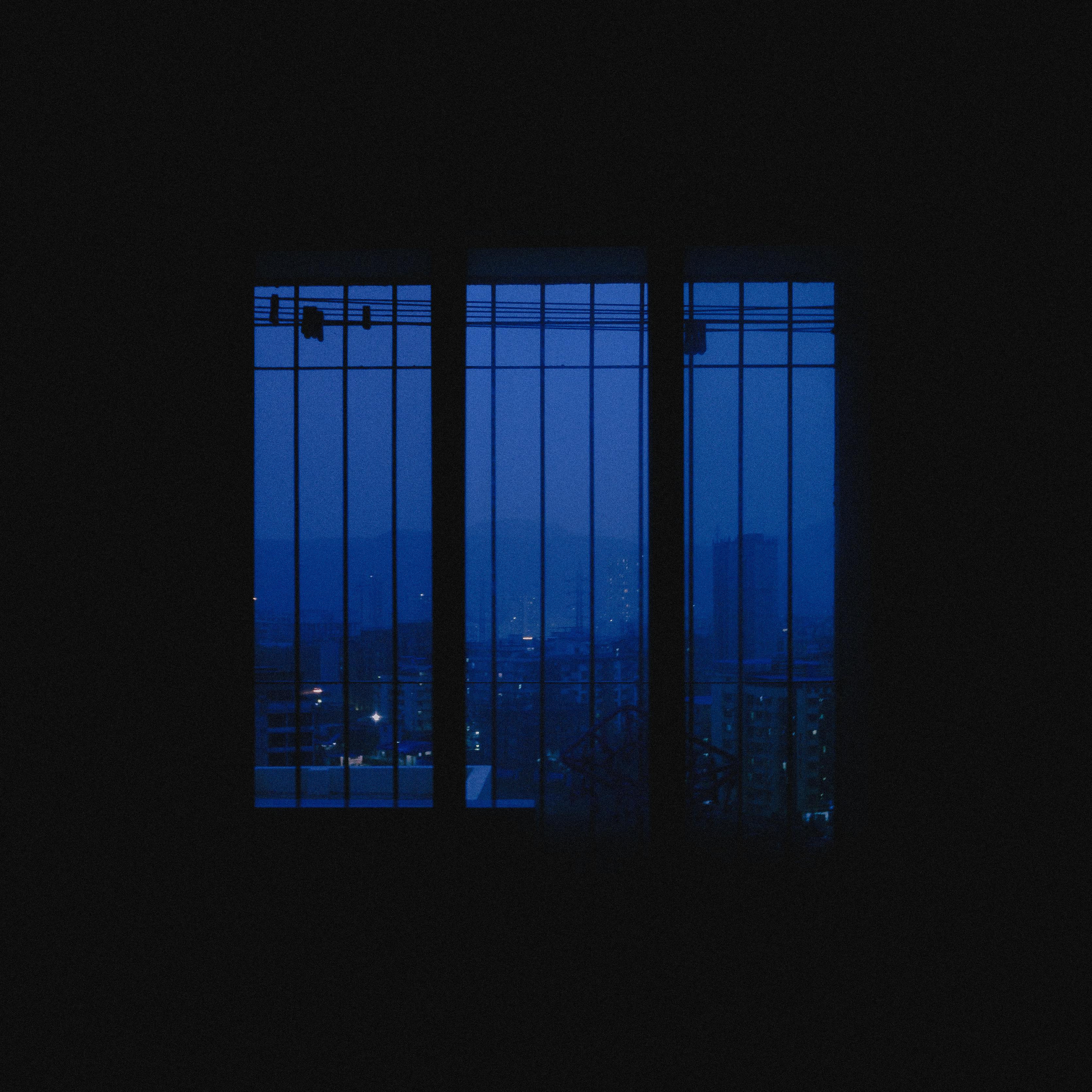Serene nighttime cityscape through a barred window with urban light glow.