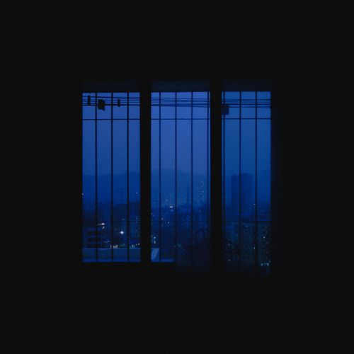 Free Serene nighttime cityscape through a barred window with urban light glow. Stock Photo