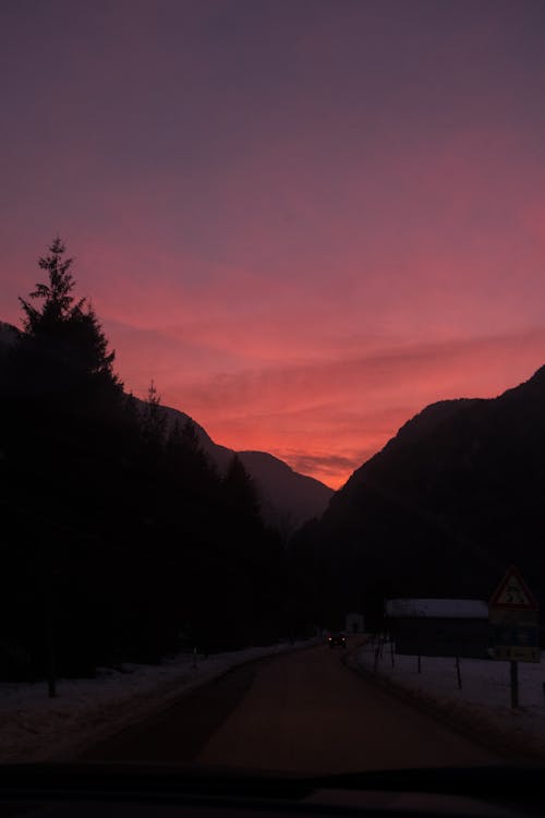 Picturesque view of fir trees and mountains against pink cloudy sunset sky in winter in middle of nowhere