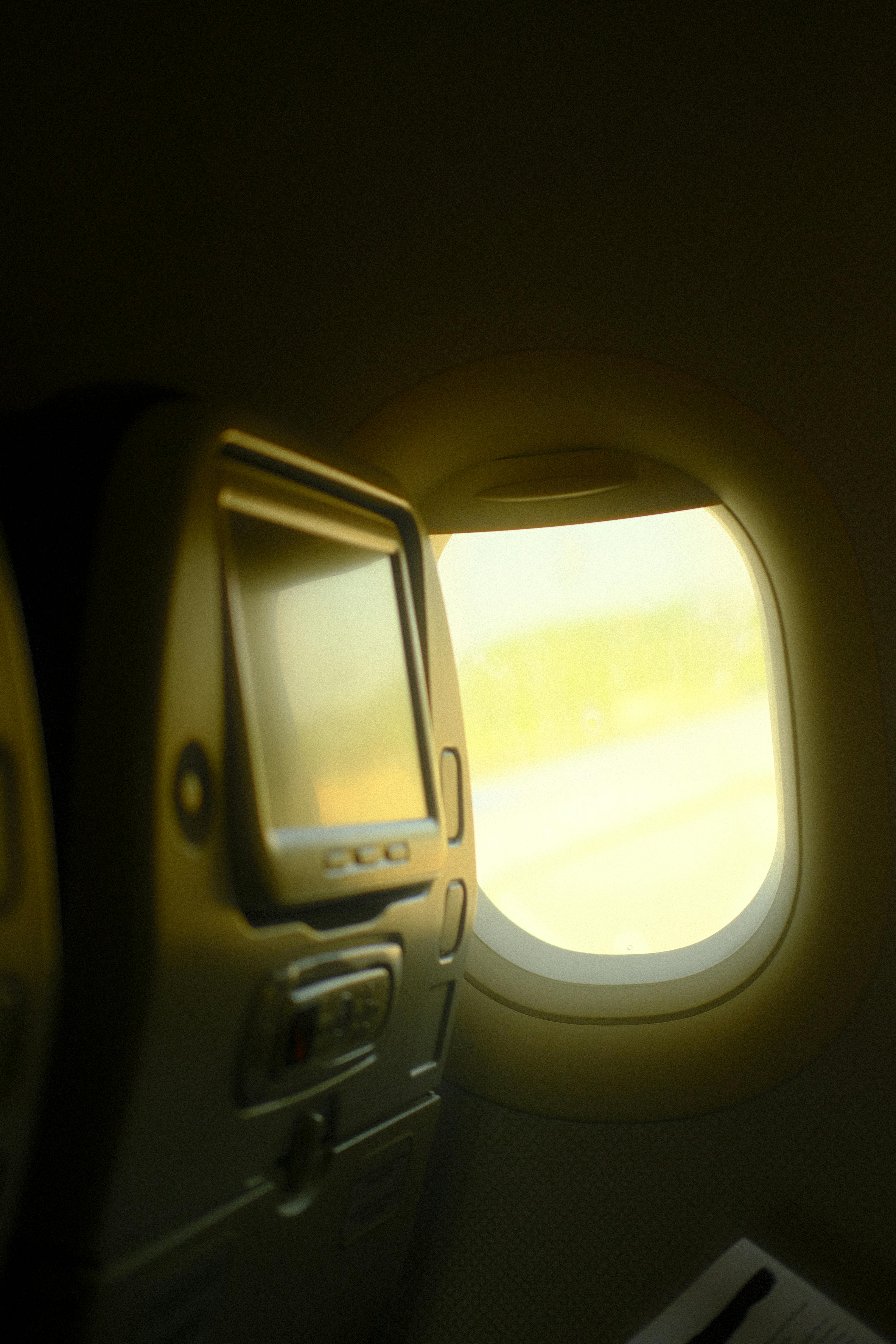 Free Passenger seat view of an airplane window with sunlight streaming in, highlighting an in-flight entertainment screen during a journey. Stock Photo