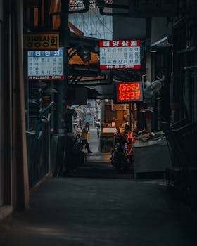 Dimly lit alley in Seoul with signs and motorbikes, capturing urban life.