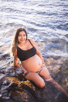 Smiling pregnant woman in swimwear enjoying the seashore during the day.
