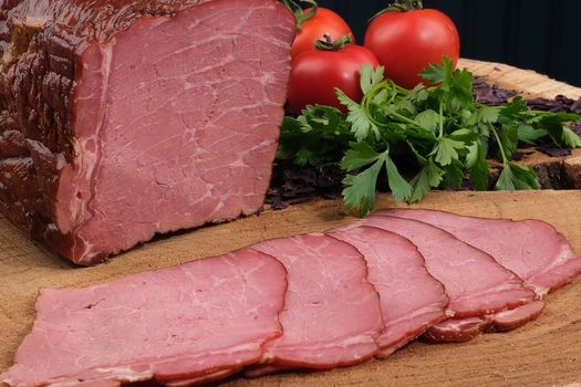 Sliced roast beef with fresh tomatoes and parsley on a wooden board.