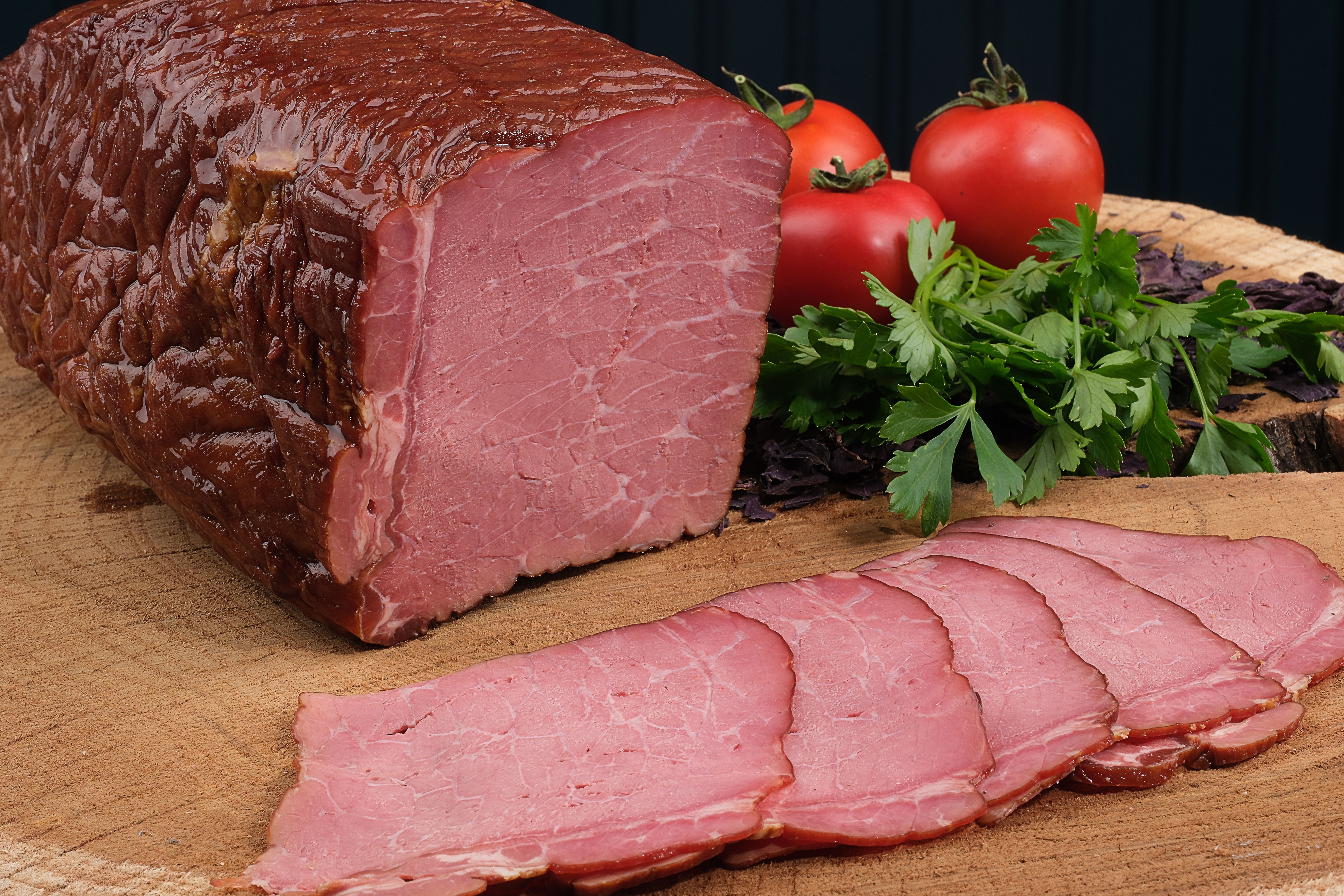 Delicious sliced roast beef on a wooden board with fresh parsley and ripe tomatoes.