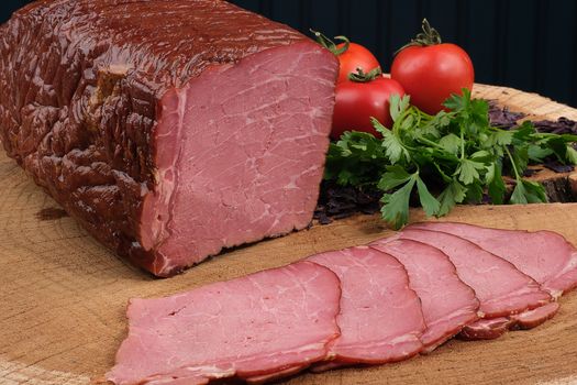 Delicious sliced roast beef on a wooden board with fresh parsley and ripe tomatoes.