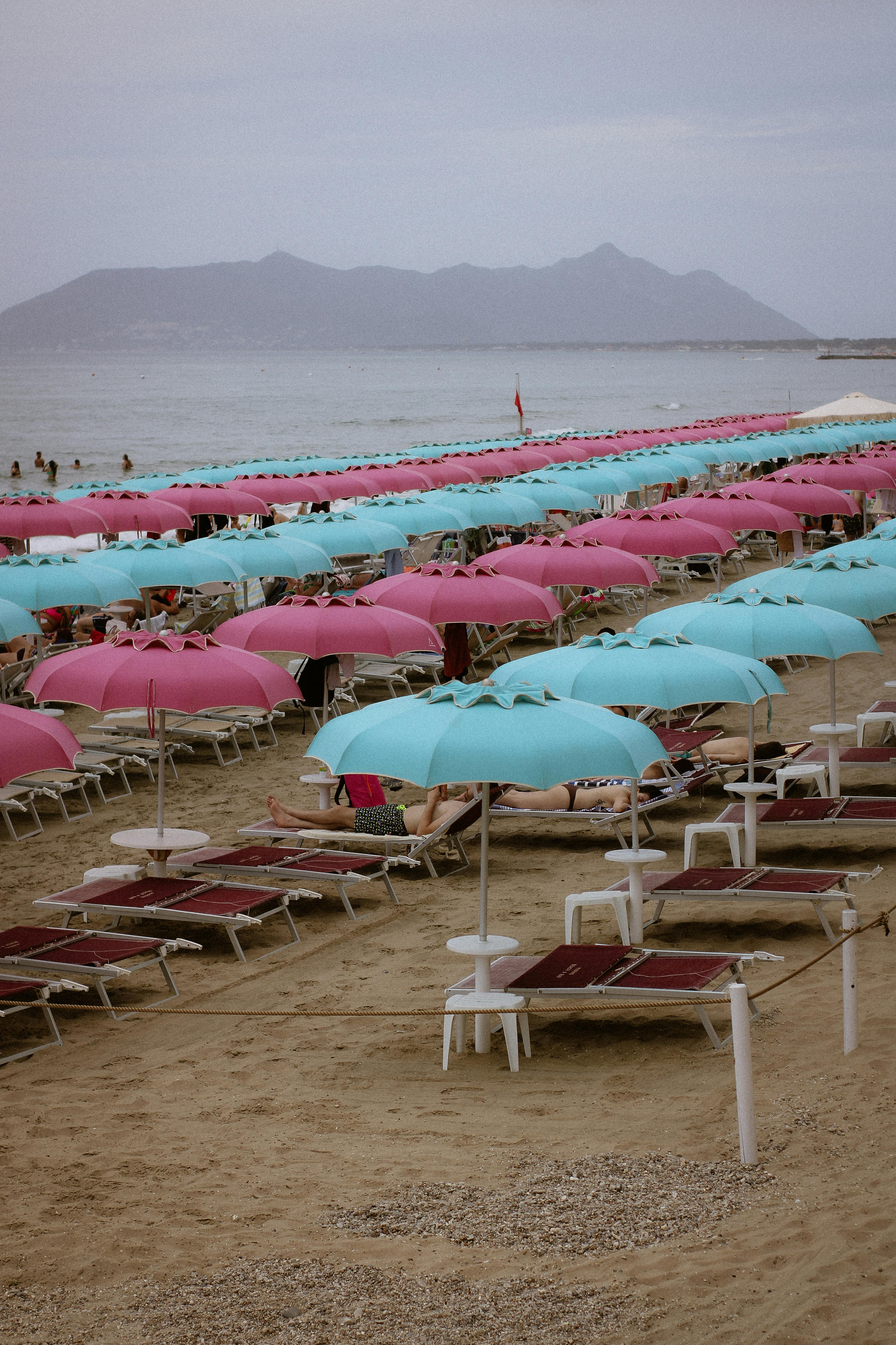 Vibrant pink and blue umbrellas line a sandy beach on a cloudy summer day, perfect for vacation inspiration.