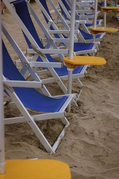 An aligned row of blue sunbeds on a sandy beach ready for summer relaxation.