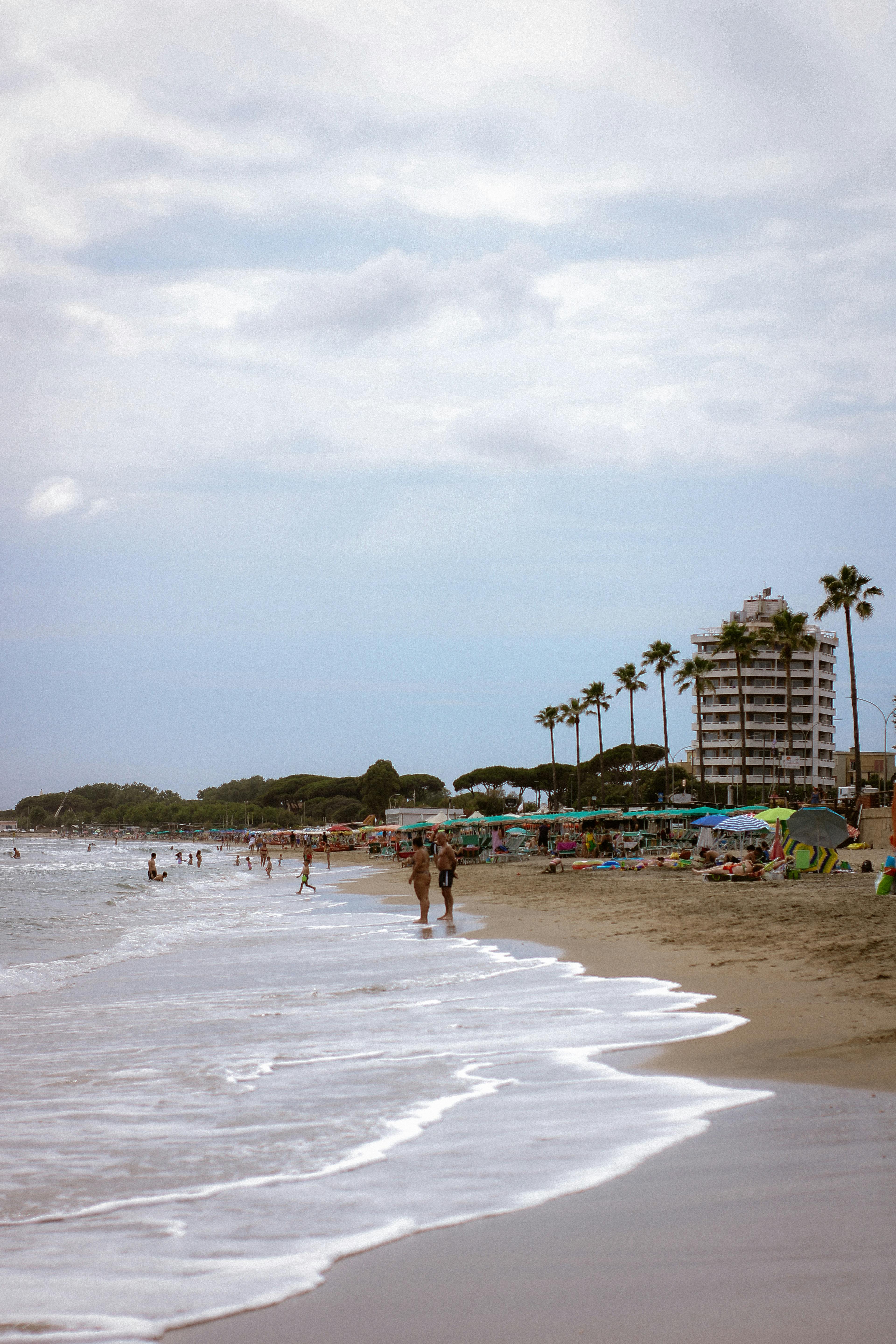 Enjoy the serene atmosphere of a sandy beach with palm trees and a towering hotel by the shore.