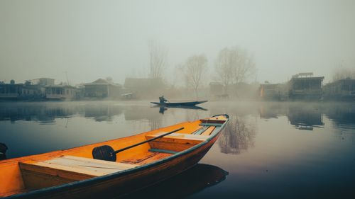 Free Foggy lake scene with a solitary rowboat in a serene village setting. Stock Photo