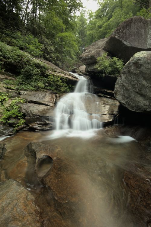 Free Serene waterfall flowing through lush forest rocks captured with a long exposure. Stock Photo