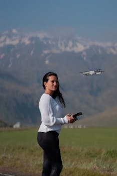 Woman operating a drone in a beautiful mountainous area with grassy fields.