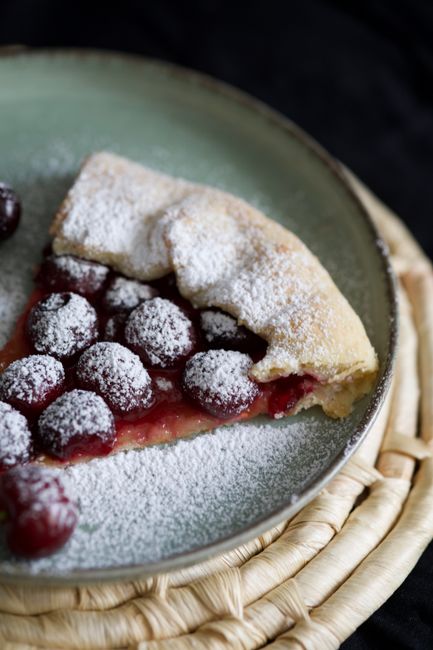 A golden lattice-topped cherry pie on a wooden table with dark red filling bubbling through the vents and a bowl of fresh whole cherries beside it.