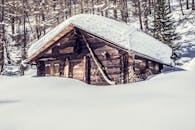 一座质朴的木制小屋坐落在宁静的冬季森林中，被积雪覆盖