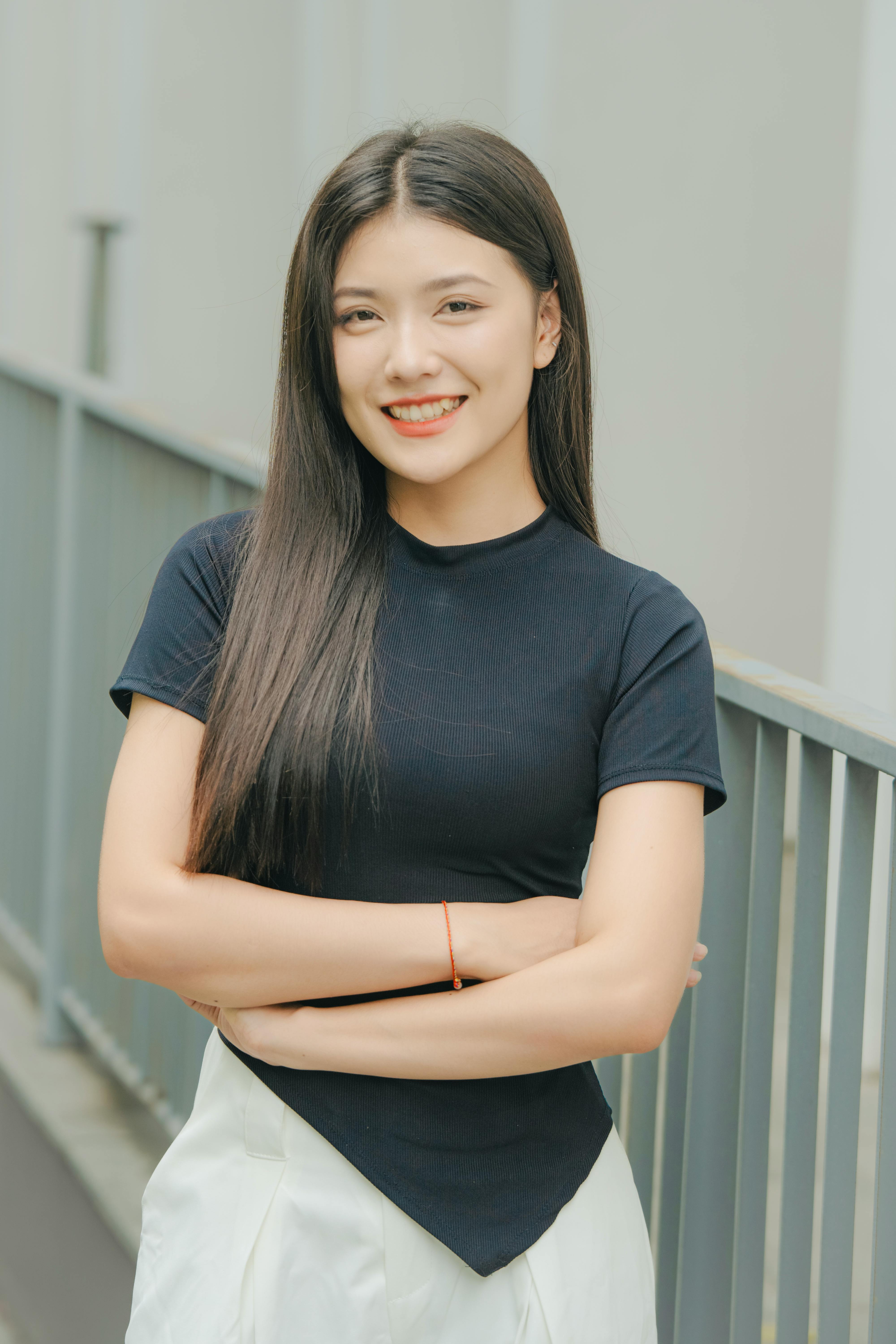 Portrait of a smiling woman with black hair, arms crossed, in an urban outdoor setting.