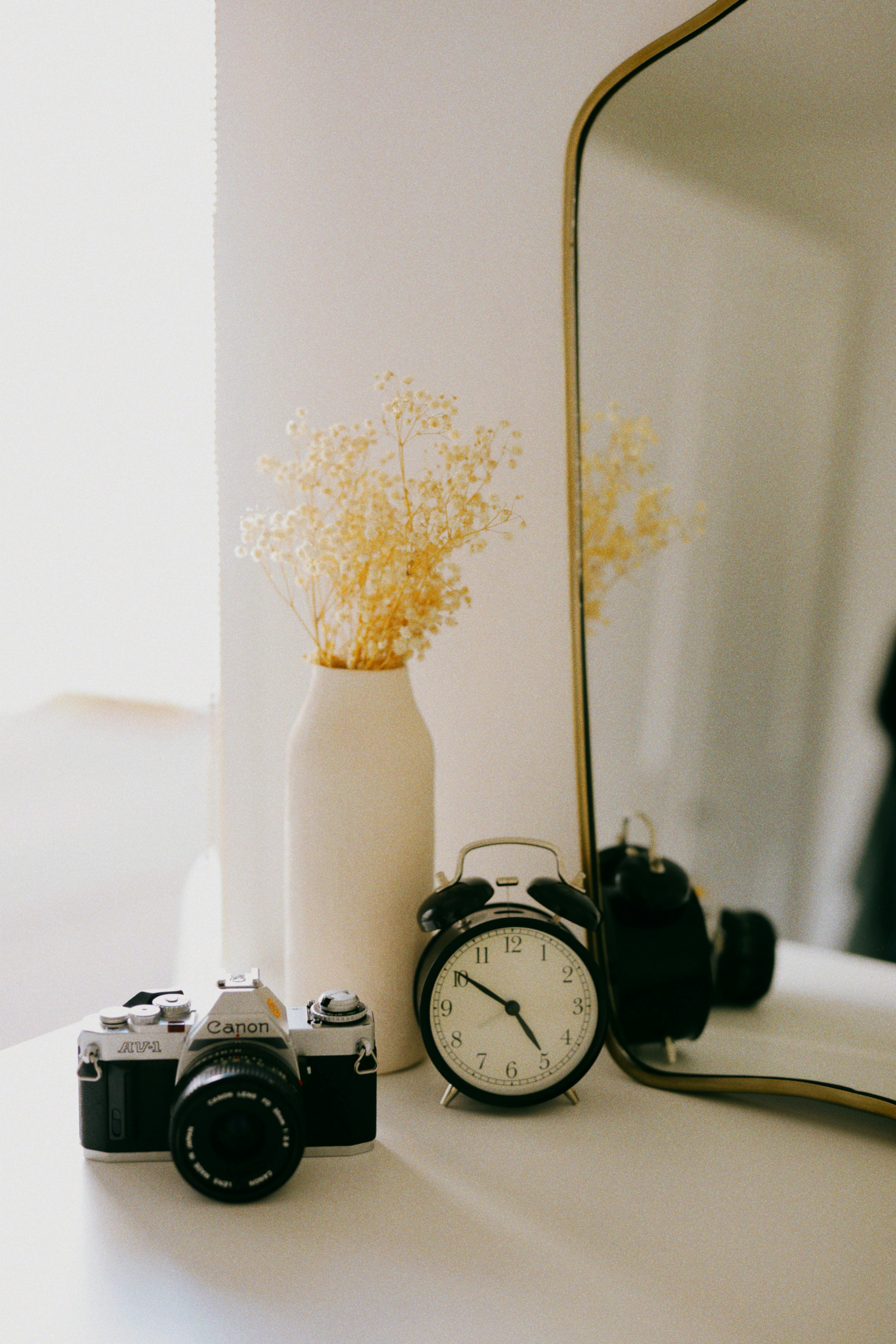 Still life of vintage camera, retro clock, and vase with dried flowers on a table.