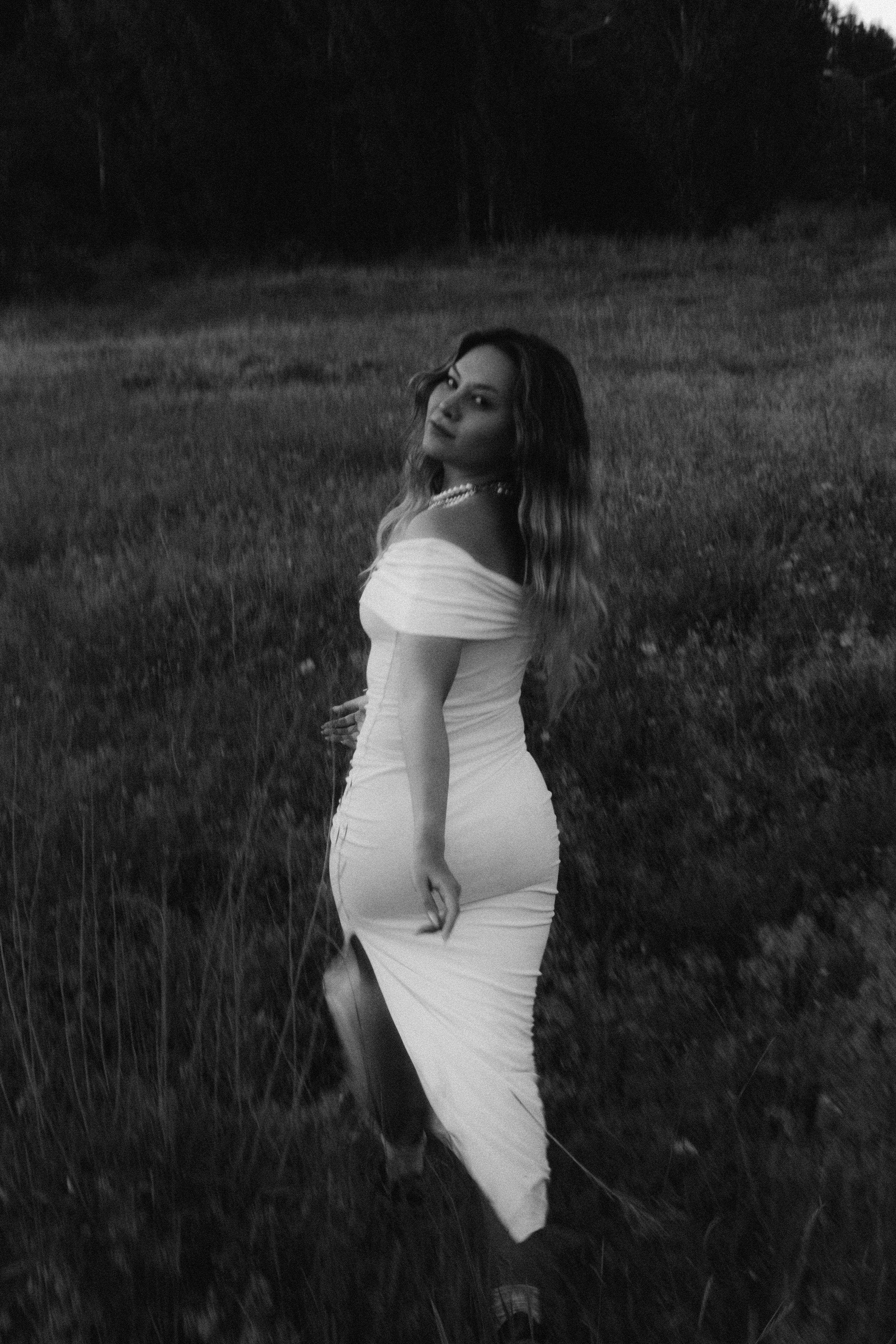 A woman in a white off-the-shoulder dress walking through a meadow.