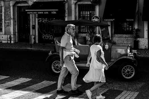 A couple crosses a Lisbon street with a vintage car in the background, capturing urban life.