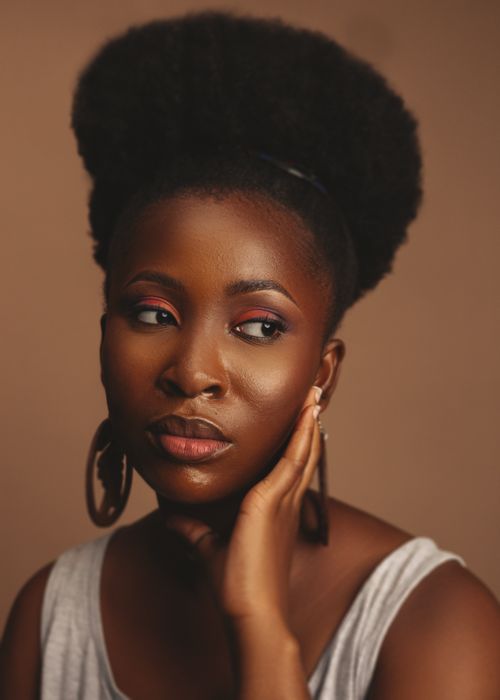 Free Studio portrait of a black woman with afro hair and earrings on a brown background. Stock Photo