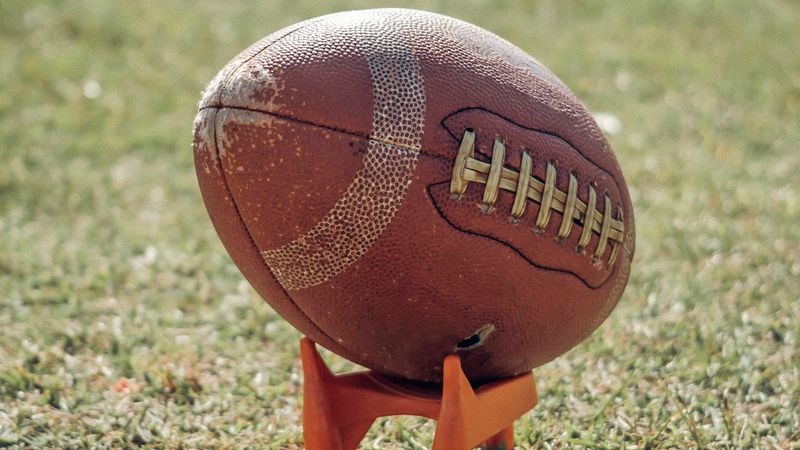 Abgenutzter brauner American Football auf einem orangefarbenen Kicking Tee im Gras