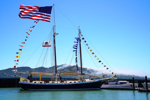 Vibrant sailboat with flags and blue sky in Tiburon, California harbor.