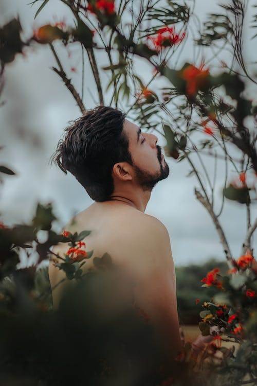 Selective Focus Photo of Shirtless Man Standing Next to Flower Plants With His Head Up and His Eyes Closed