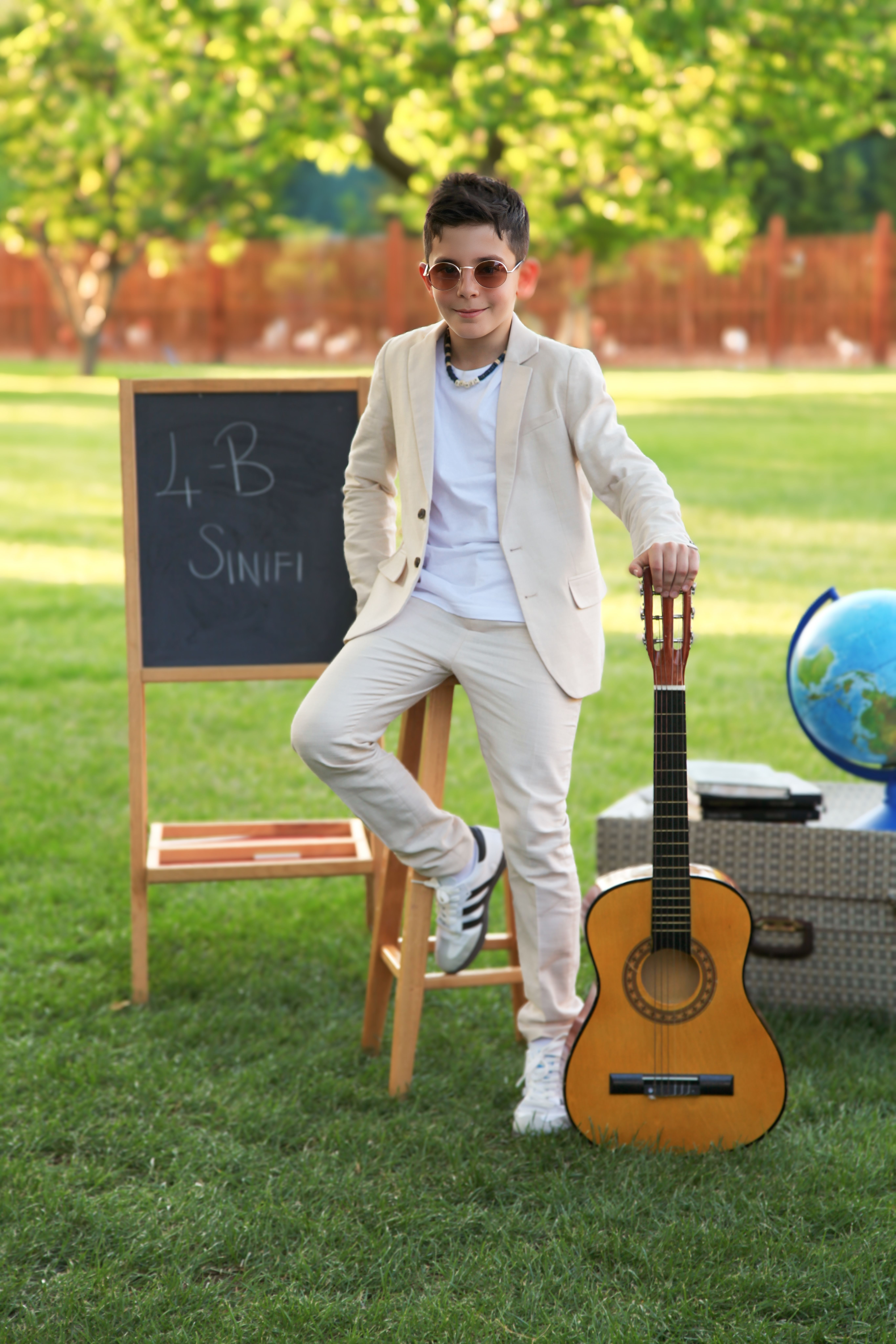 Boy in stylish outfit poses with guitar and blackboard outdoors on a sunny day.