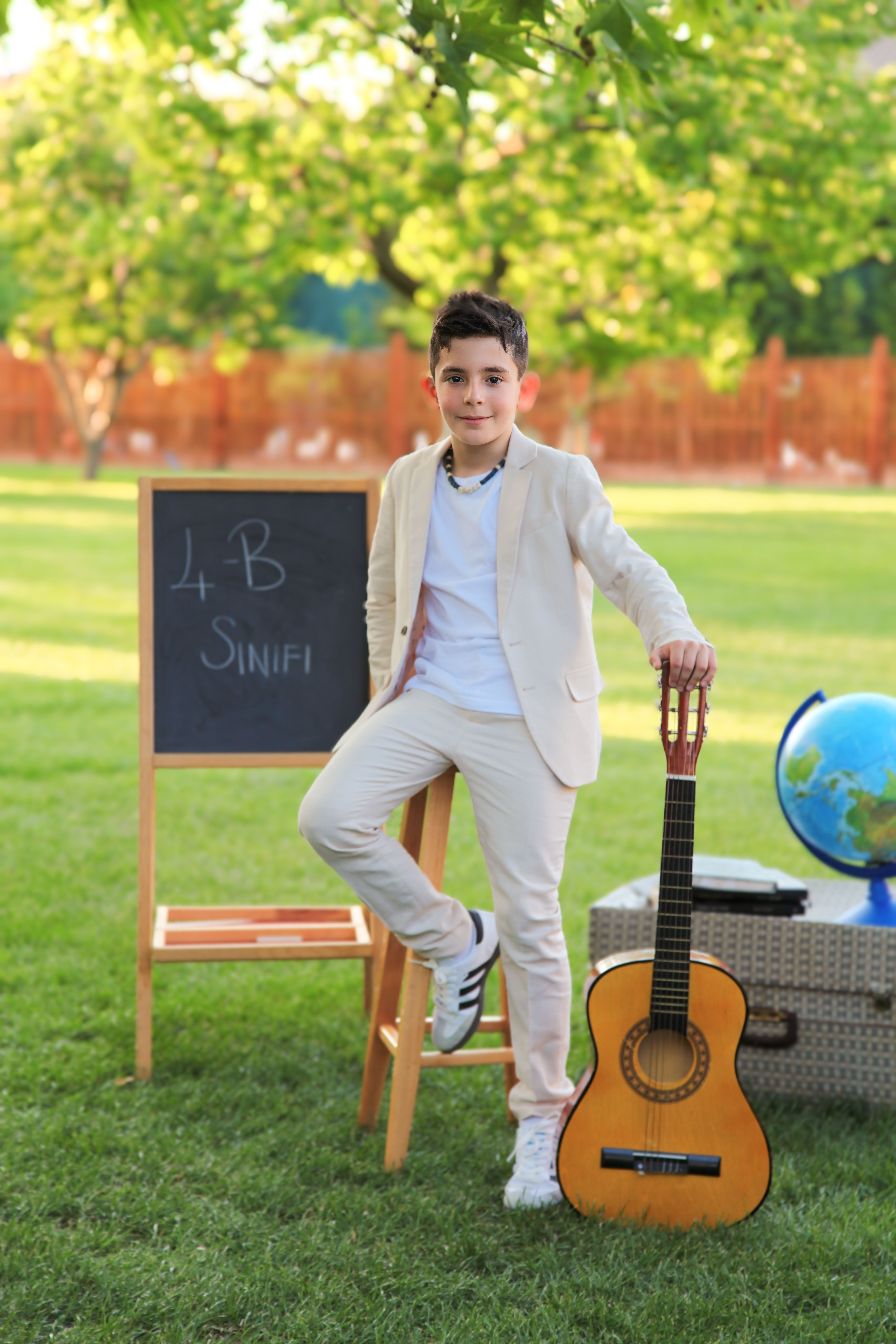 A stylish young boy poses confidently outdoors with a guitar and blackboard in the background.