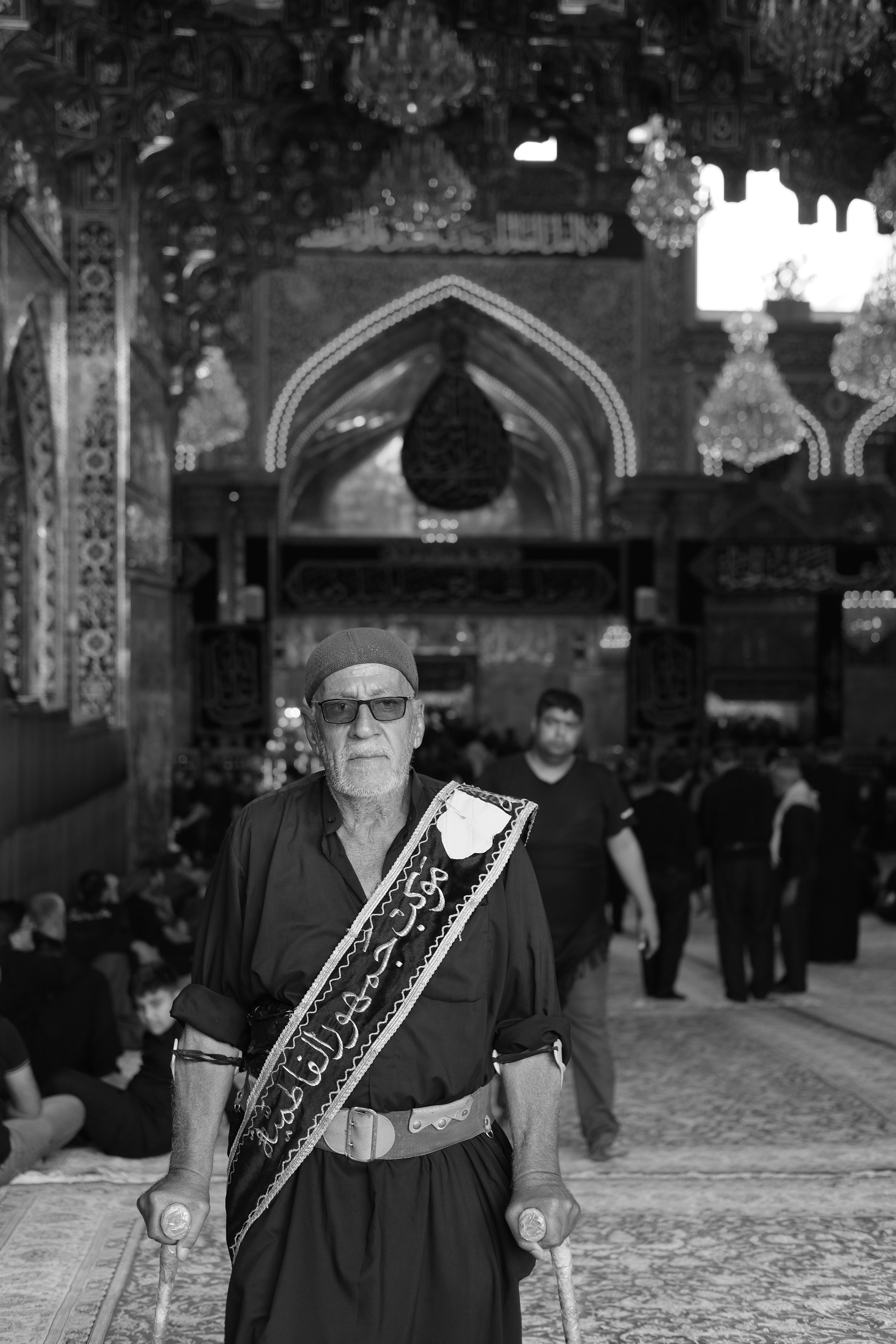 Elderly man with crutches in a mosque, part of a religious gathering.