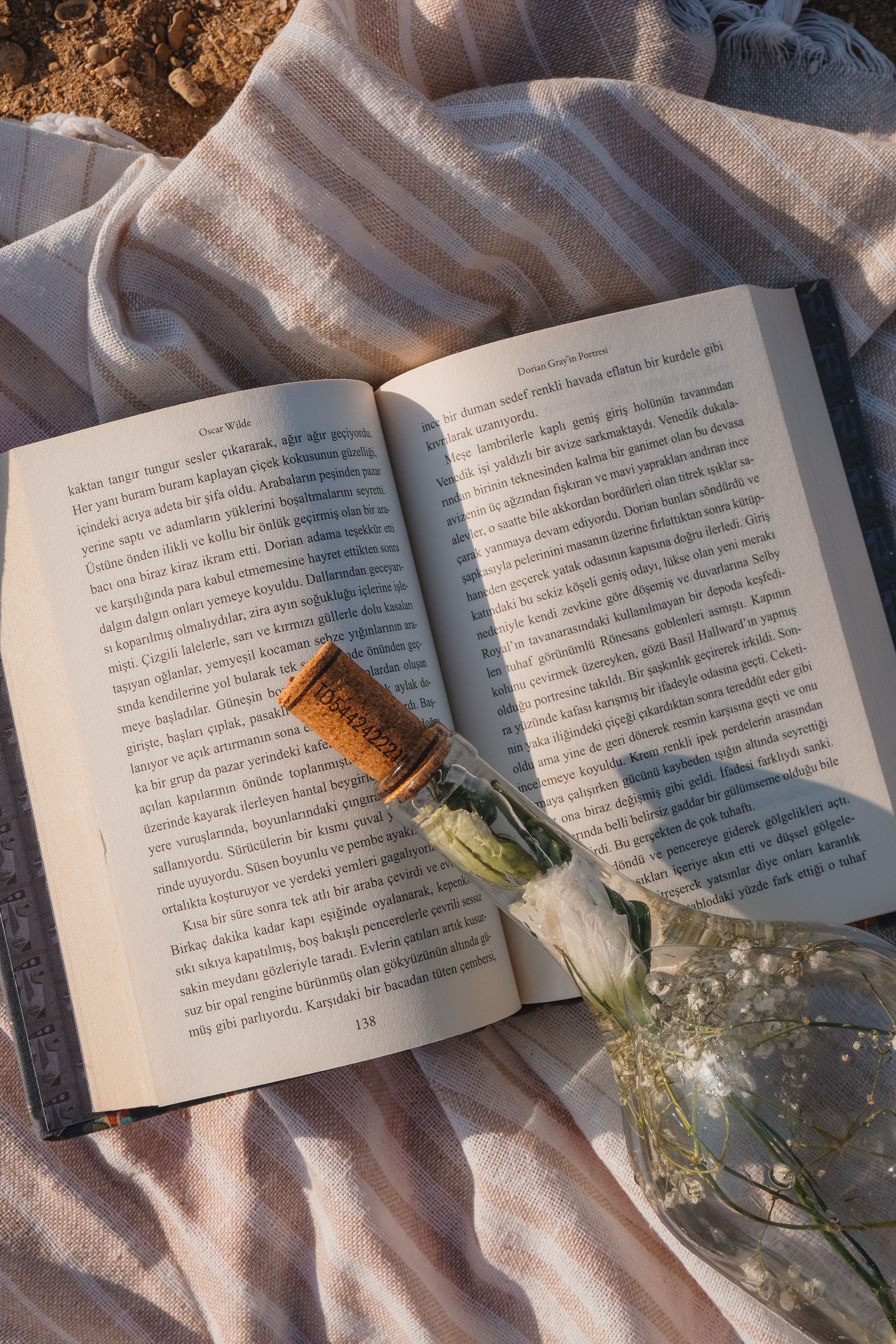 Open book on striped blanket with glass bottle, creating a cozy picnic atmosphere.