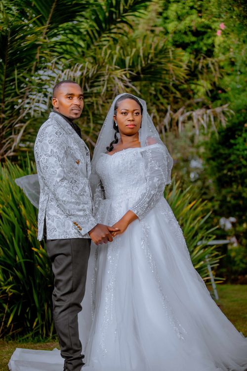 Free Black bride and groom posing outdoors in a lush garden setting, showcasing wedding attire. Stock Photo