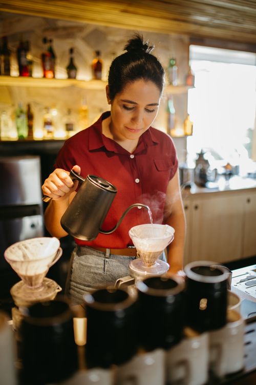 Free A barista in a red shirt makes pour-over coffee in a cozy café setting. Stock Photo
