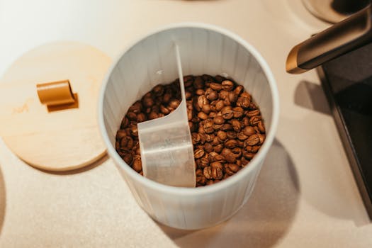 High angle shot of coffee beans in a white container with a scoop, perfect for coffee lovers.