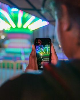 A person uses a phone to capture bright, colorful carnival lights at night.