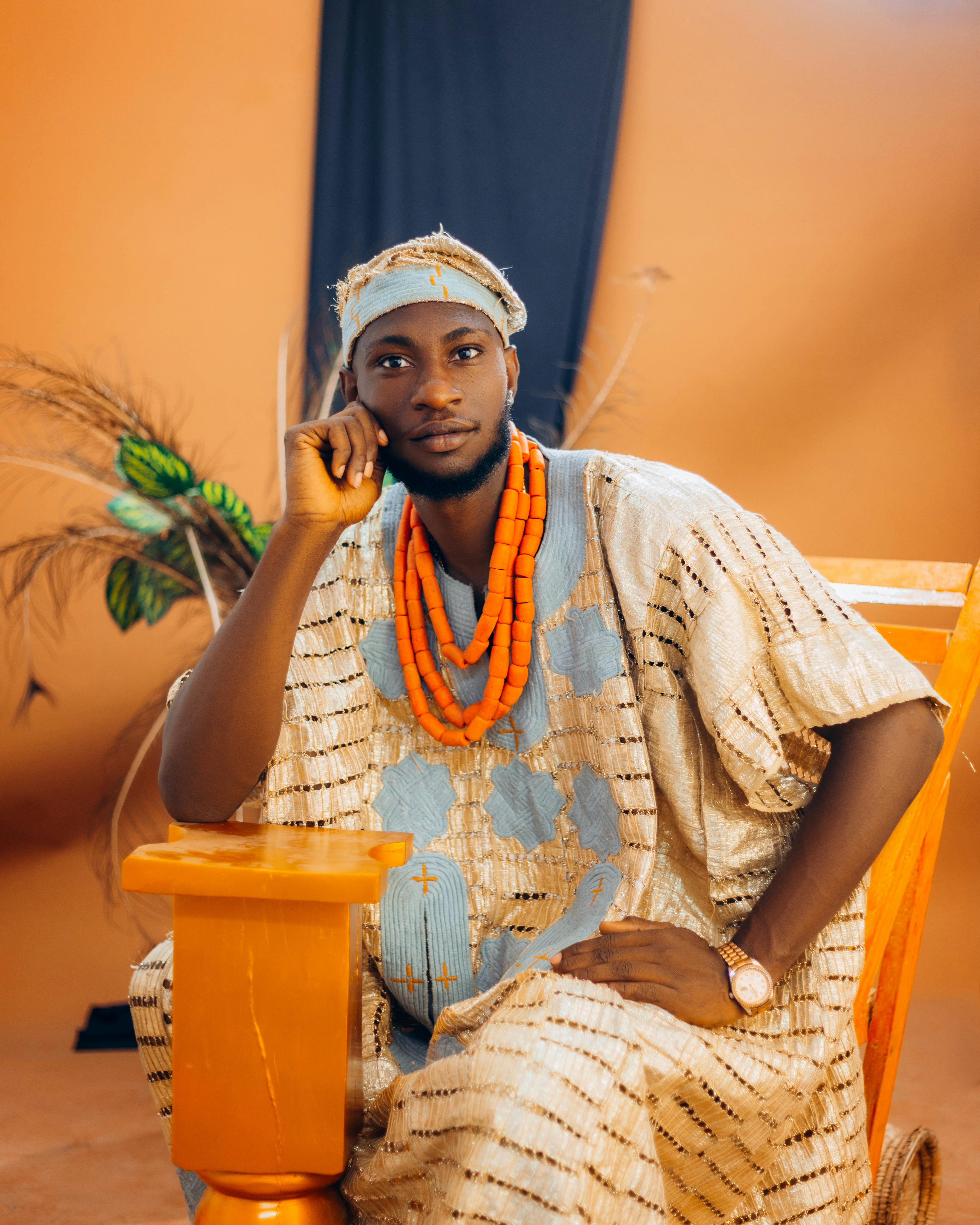 A man in cultural attire sits elegantly, showcasing traditional fashion with vibrant jewelry.