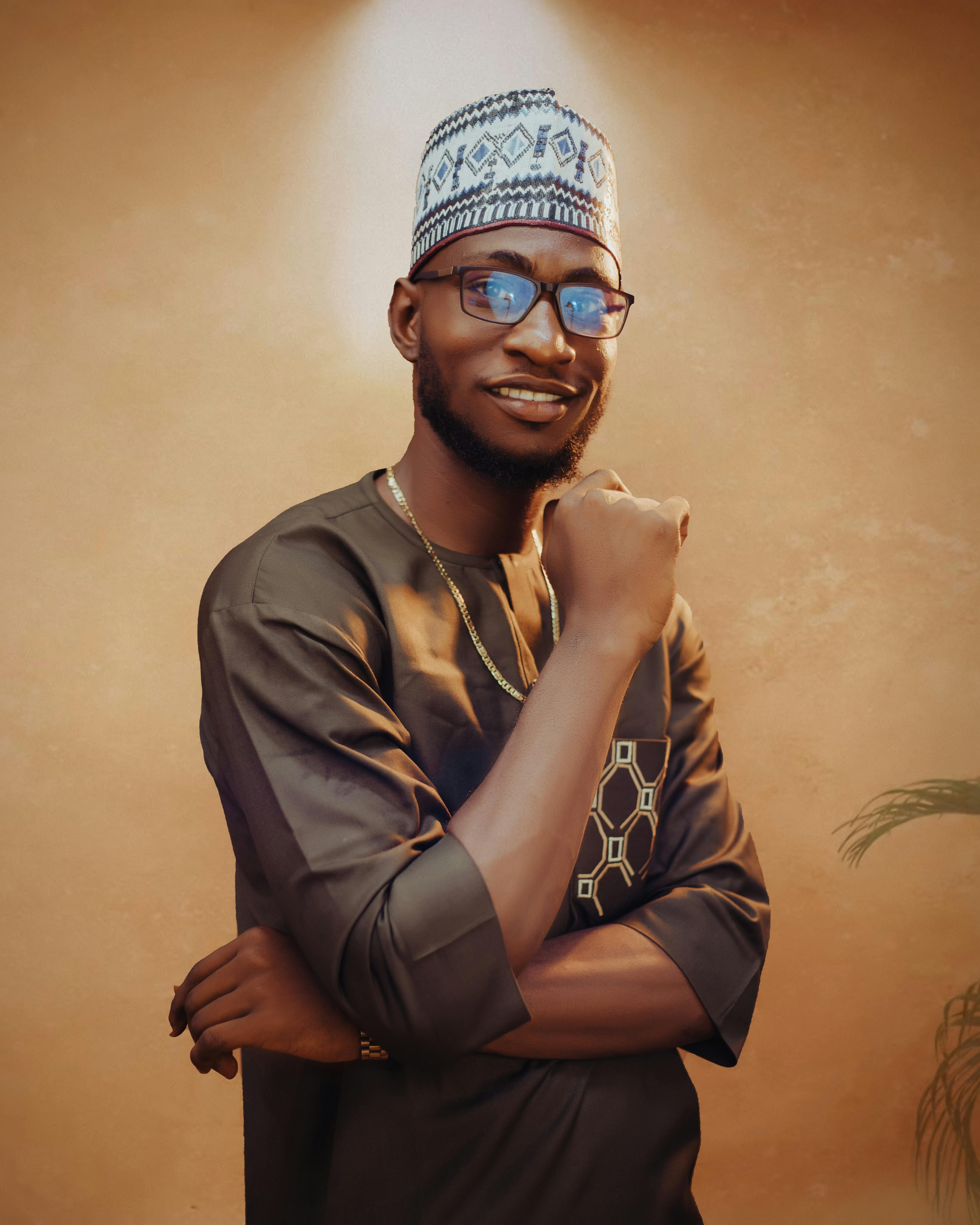 Confident African man with glasses and hat, wearing traditional attire and smiling warmly.