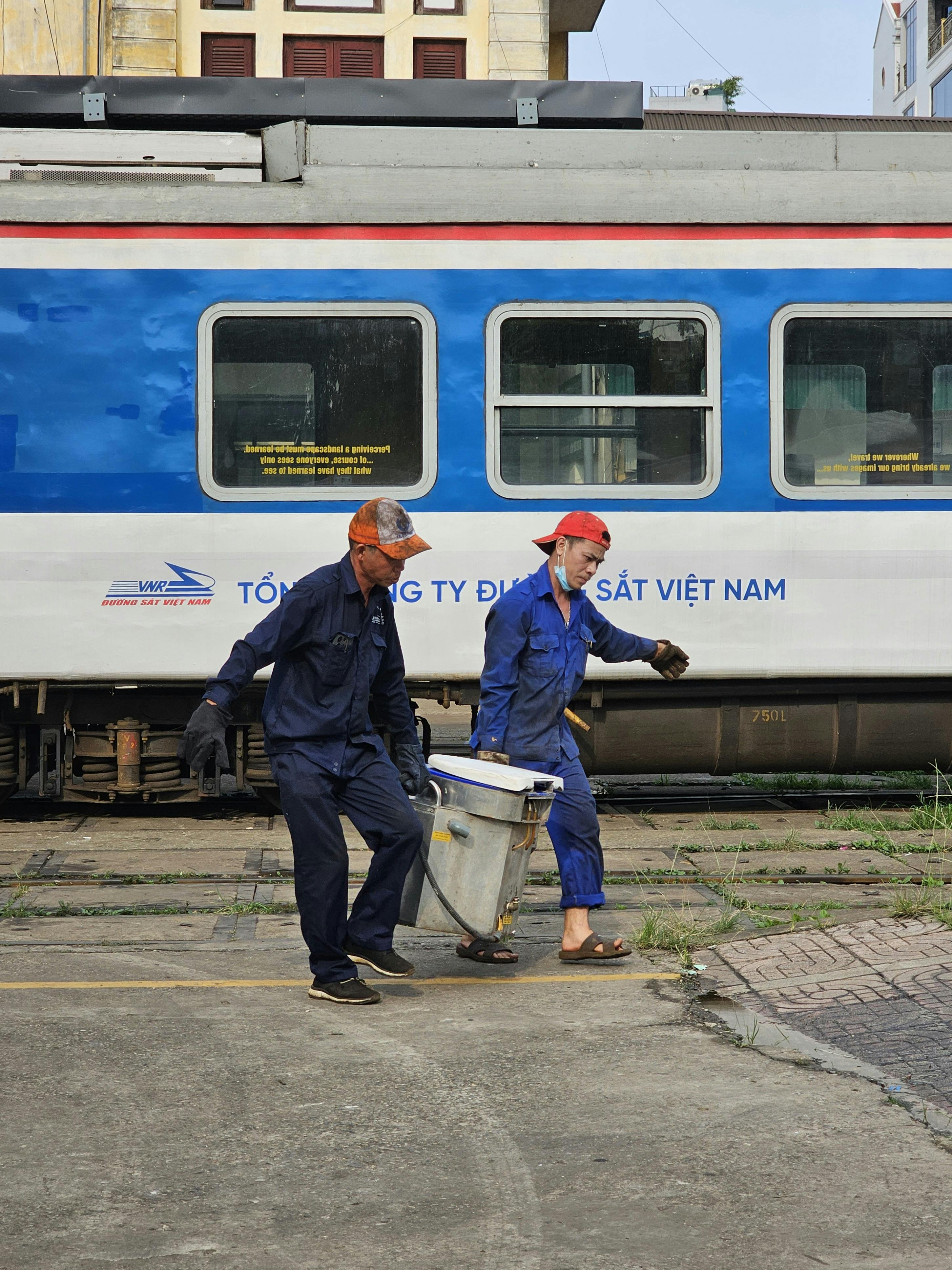 two men carrying a box in front of a train