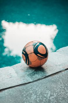 A soccer ball rests on the edge of a swimming pool under clear skies, evoking relaxation.