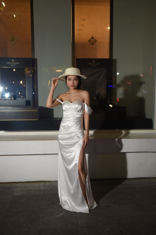 Free Chic woman in a white gown and hat posing elegantly outside a store at night. Stock Photo