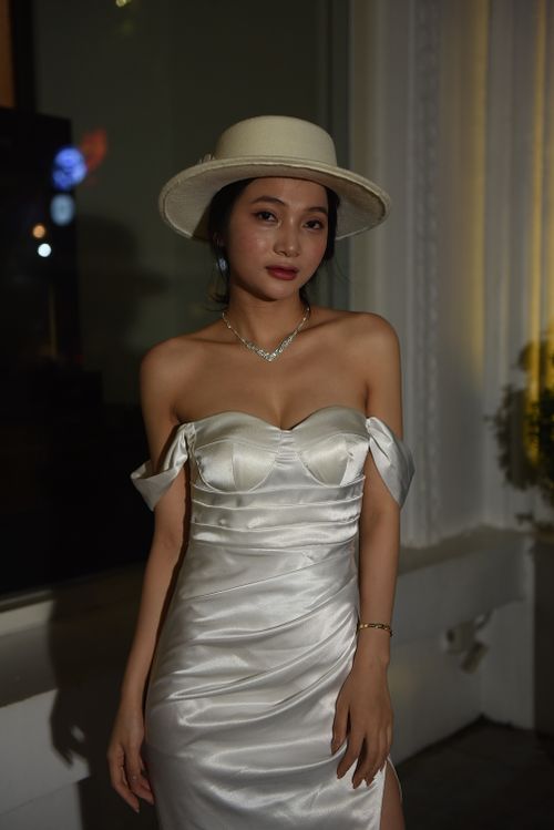 Free Stylish woman in a white dress and hat posing elegantly indoors at night. Stock Photo