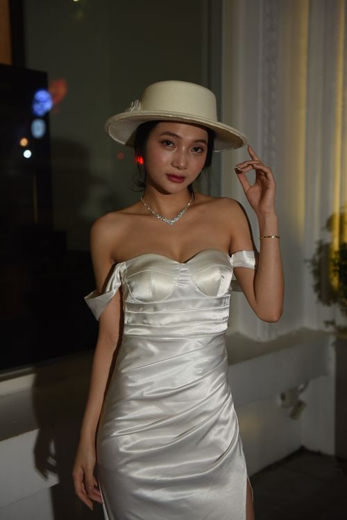 Free Portrait of a young woman in an elegant white dress with a matching hat, indoors at night. Stock Photo
