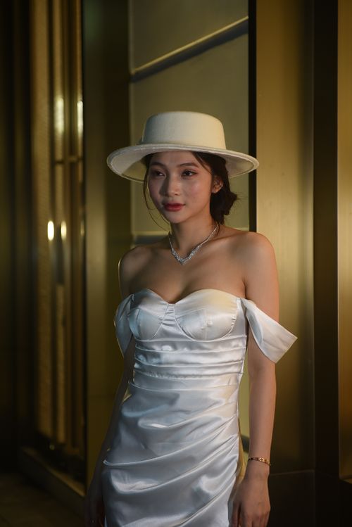 Free Elegant woman in a white dress and hat posing stylishly in an urban setting at night. Stock Photo
