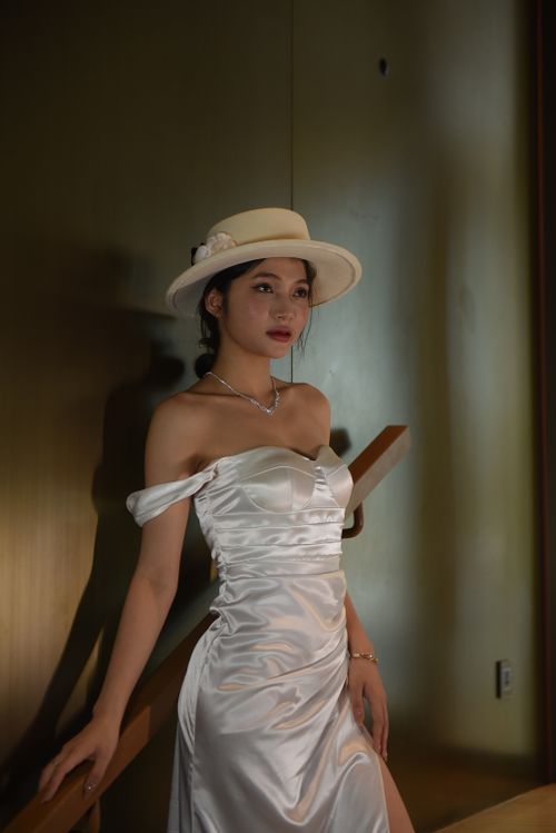 Free Serene portrait of an elegant woman in a white dress and hat, exuding sophistication. Stock Photo