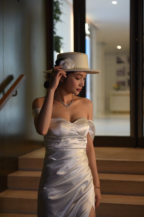 Free Graceful Asian woman in white dress and hat, captured in an elegant indoor setting. Stock Photo