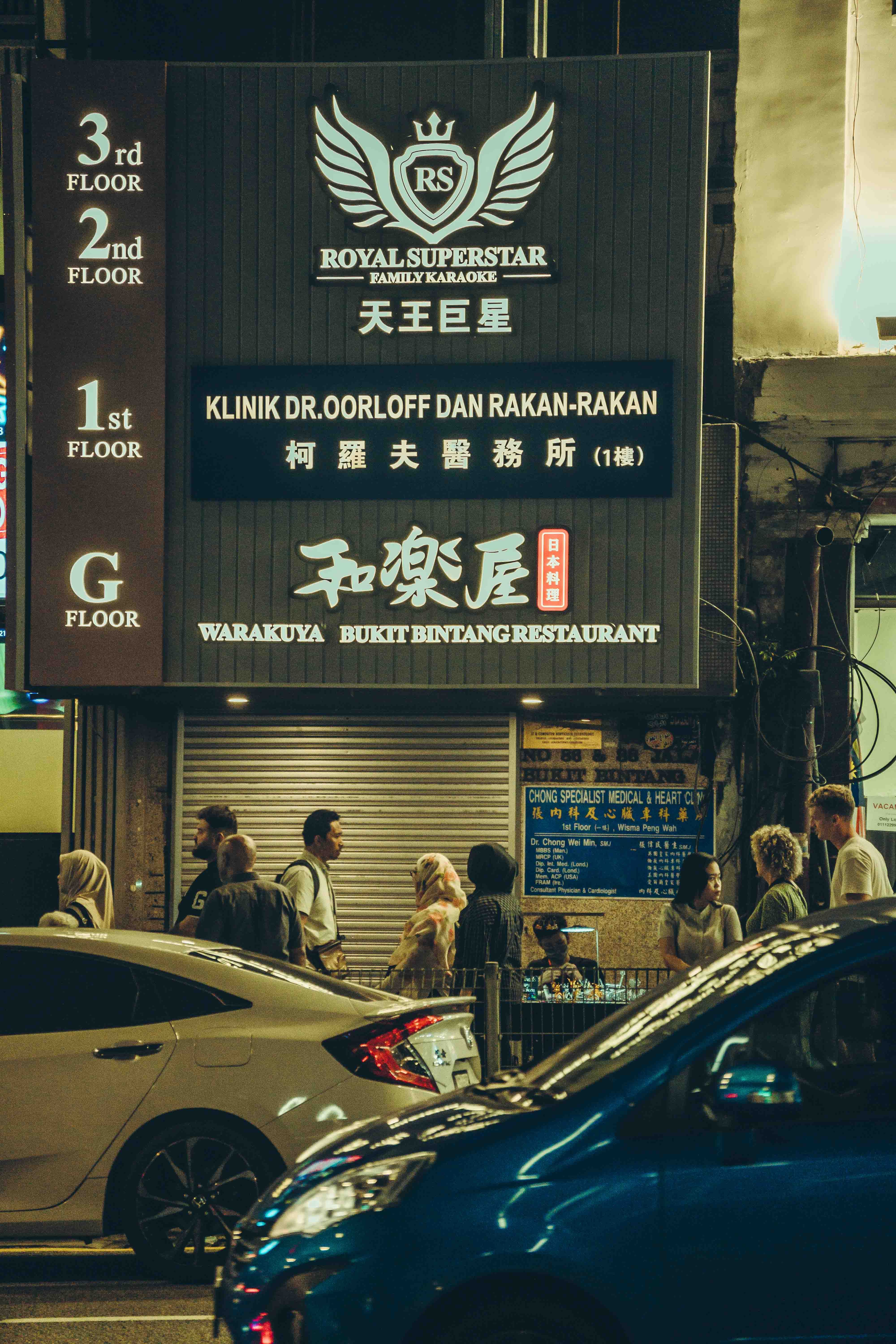 Bustling night scene in Kuala Lumpur with pedestrians and cars on urban streets.