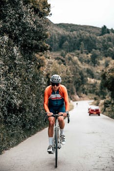 Male cyclist riding on a rural road through lush hills, wearing sportswear and helmet.
